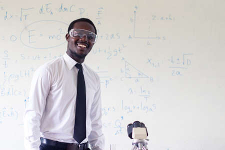 Science african teacher standing in front of blackboard teaching student in classroomの写真素材