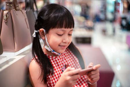 Little child girl playing with smartphone in modern commercial supermarket center