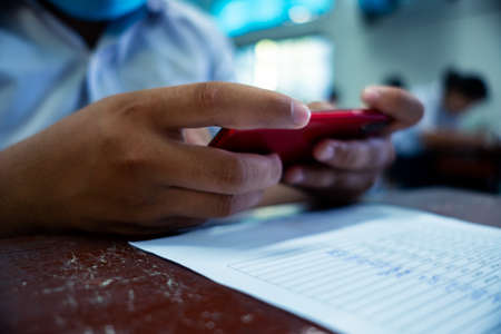 Students using smartphone and doing exam answer sheets exercises in classroom of schoolの写真素材