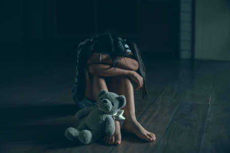 Sad little child girl sitting alone with teddy bear on floorの写真素材