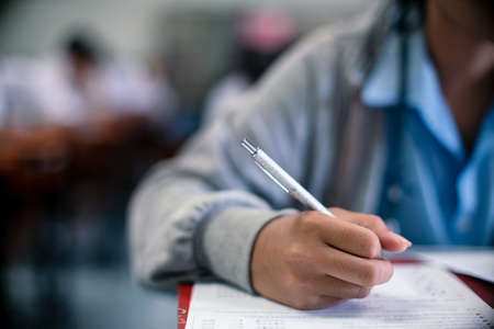 Students writing and reading exam answer sheets exercises in classroom of school with stressの写真素材