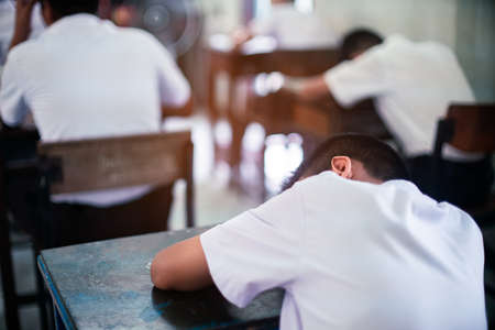 Tired uniform student sleeping in a exam test classroomの写真素材