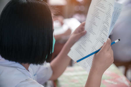 Student  wearing mask for protect  corona virus or covid-19 and doing exam answer sheets exercises in classroom of school with stress.の写真素材