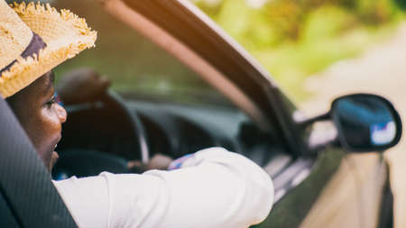 African man driver wearing a hat and smiling while sitting in a car with open front window