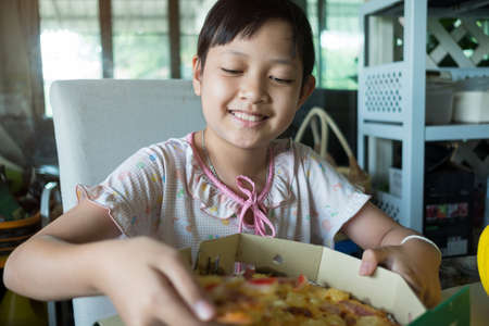 Asian little girl eating pizza at homeの写真素材