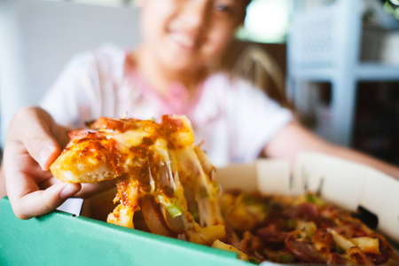 Asian little girl eating pizza at homeの写真素材
