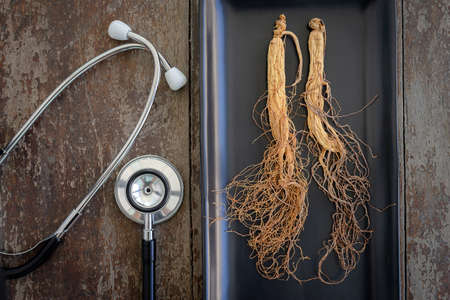 Dry ginseng on black plate with stethoscope on the wood background
