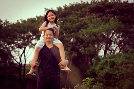 Asian little child girl riding on father's shoulders in the green natural background.Vintage color styleの写真素材