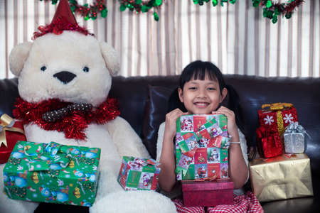 Xmas Festive asian little girl smiling and holding a gift box at homeの写真素材