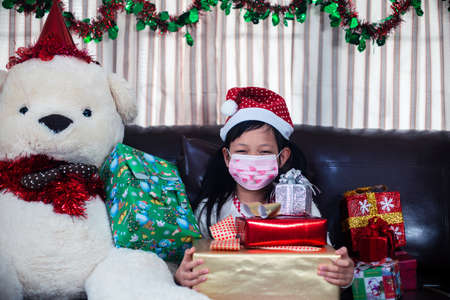 Xmas Festive asian little girl wearing face mask and holding a gift box at homeの写真素材