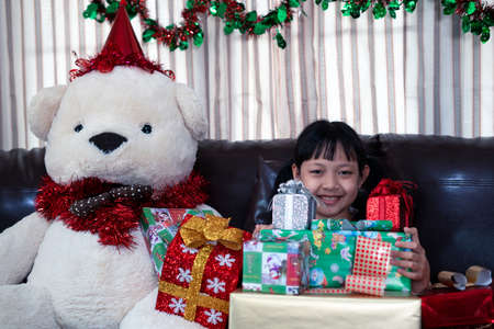 Xmas Festive asian little girl smiling and holding a gift box at homeの写真素材