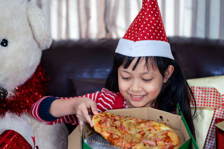 Happy asian child girl eat pizza in the room decorated for the new year. Christmas dinner fast foodの写真素材