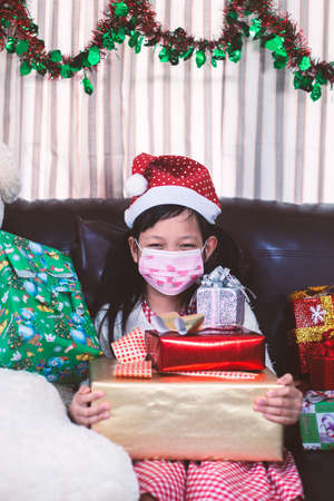 Asian little girl holding a gift box with wear face mask in christmas dayの写真素材