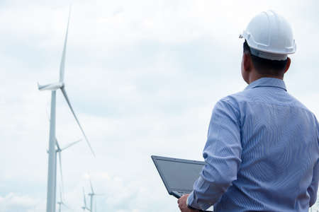 Engineers windmills are working on laptop with the wind turbine in backgroundの写真素材