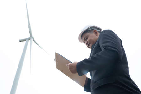 Engineers windmills wearing face mask and  working on clipboard against wind turbineの写真素材