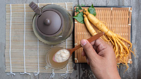 Hand of man holding a spoon with ginseng powder for tea on a wooden tableの写真素材