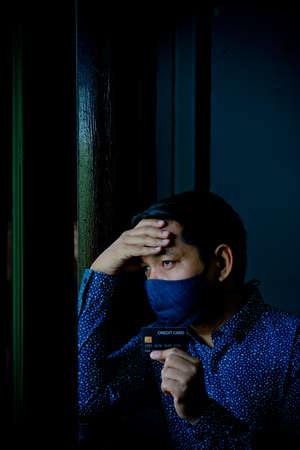 Sad confused and stress man holding credit cards with wearing face mask.Low key style