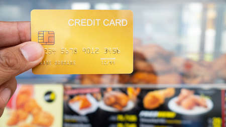 Hand holding the credit card with fried chicken shop in background.16:9 styleの写真素材