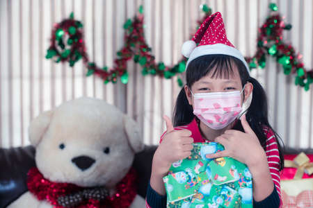 Asian little girl holding a gift box with wear face mask in christmas dayの写真素材