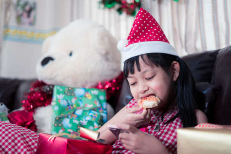 Happy asian child girl eating pizza and using smartphone in the room decorated for the new year. Christmas dinner fast foodの写真素材