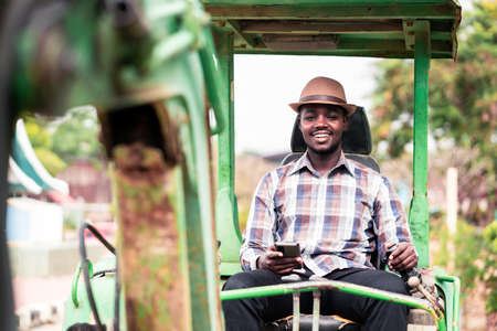 African worker driving heavy construction equipment backhoe with using smartphoneの写真素材