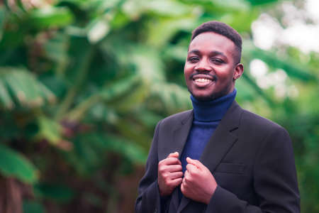 Handsome african business man standing in trendy formal black suit. Guy with beard wearing blue long sleeve or sweaterの写真素材
