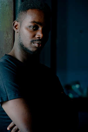 Sad african man standing in dark room. Depression and anxiety disorder conceptの写真素材
