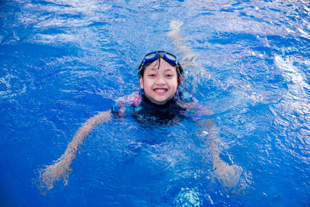 Pretty little girl in swimming pool with smile and happy in summertimeの写真素材
