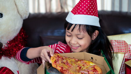 Happy asian child girl eat pizza in the room decorated for the new year. Christmas dinner fast food.16:9 styleの写真素材