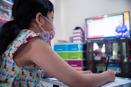 Little child girl learning on TV or smart phone at home with wearing face mask,Social distance during quarantine, Online education conceptの写真素材