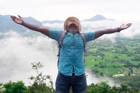 Freedom african  man traveler and hiker with backpack at the top of the hill covered with mistの写真素材