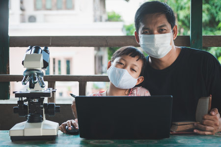 Smiling father and daughter wearing face mask and learning from home with laptop and microscope.Coronavirus or Covid-19 Outbreak school shutdownsの写真素材
