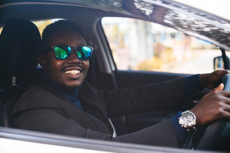 African man in a black suit sitting behind the wheel with smile and happyの写真素材