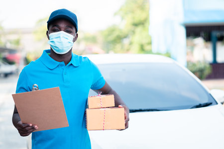 African delivery man holding boxs and cardboard with wearing face maskの写真素材