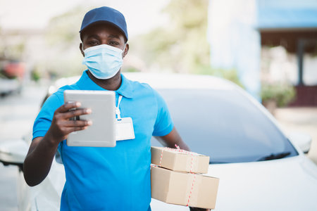 African delivery man holding boxs and tablet with wearing face maskの写真素材