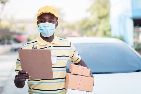 African delivery man holding boxs and cardboard with wearing face maskの写真素材