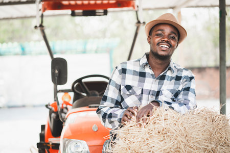 African farmer standing with rice straw bales and tractor. Agriculture or cultivation conceptの写真素材
