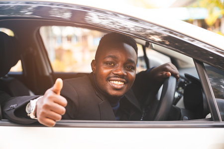 African man in a black suit sitting behind the wheel with smile and happyの写真素材