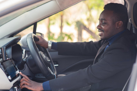African man in a black suit sitting behind the wheel with smile and happyの写真素材