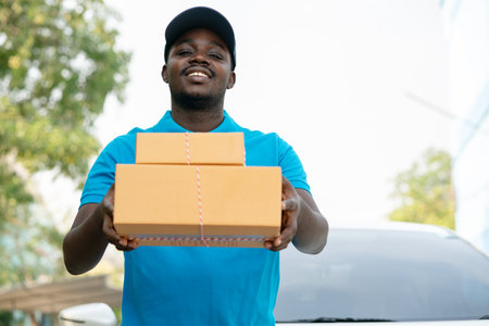 African male postal delivery courier man holding delivering package boxs in front of carの写真素材