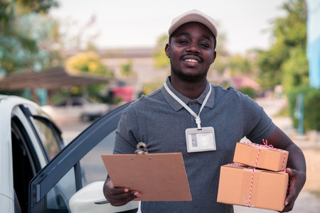 African male postal delivery courier man holding delivering package boxs and cardboard in front of carの写真素材