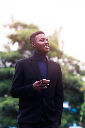 Handsome african business man using smartphone in trendy formal black suit. Guy with beard wearing blue long sleeve or sweaterの写真素材