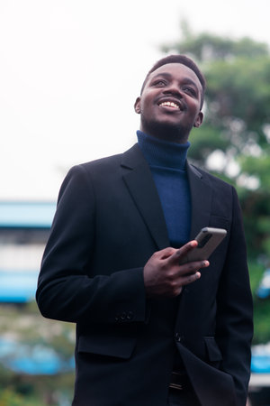 Handsome african business man using smartphone in trendy formal black suit. Guy with beard wearing blue long sleeve or sweaterの写真素材