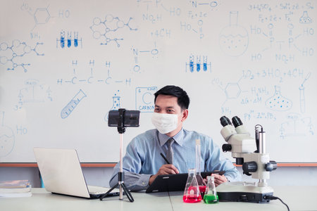 Science chemistry teacher wearing mask and   teaching online with smartphone in the classroomの写真素材