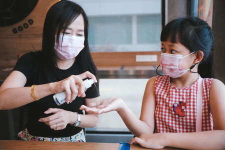 Asian mother and daughter wearing mask using  alcohol spray for prevent the  Covid-19の写真素材