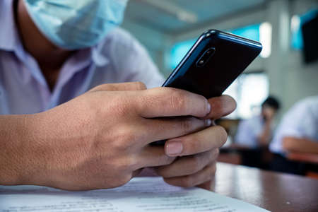Uniform students are test exam and study online by using smartphone and wearing protective facemask in classroomの写真素材