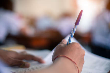 Hand of student is taking exam and writing answer in classroom for education test conceptの写真素材