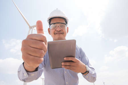 Engineer windmills are working on tablet PC with the wind turbine in background