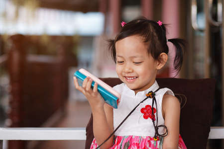 Cute little child girl playing smart phone with happy at homeの写真素材