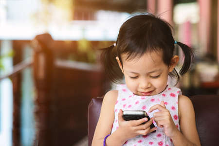 Cute little child girl playing smart phone with happy at homeの写真素材